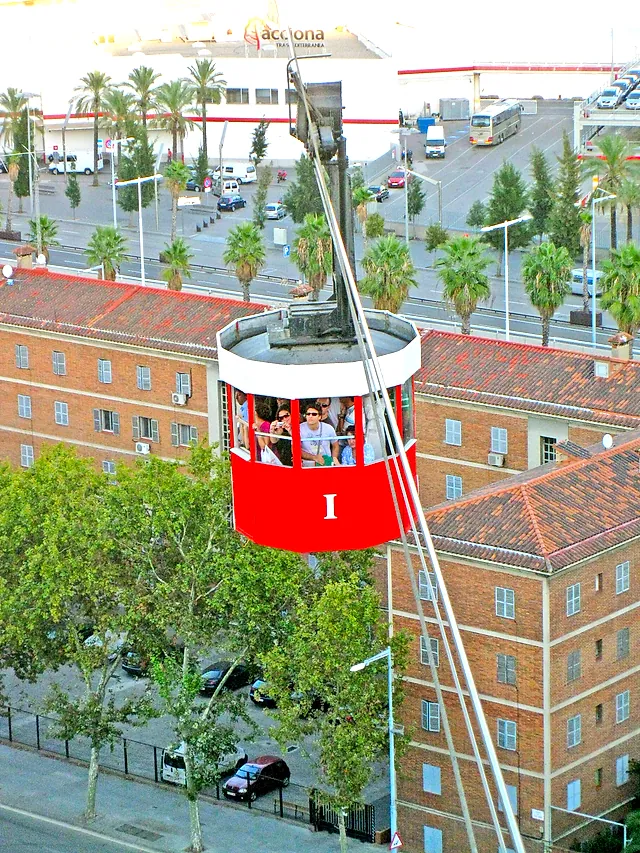 Una cabina rossa del Telefèric del Port sospesa sopra gli edifici del porto