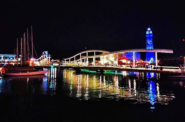 La passerella della Rambla de Mar e la torre di Jaume I illuminata, riflesse nell'acqua del Port Vell di notte